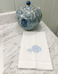 white guest towel with embroidered blue hydrangea with blue and white chinoiserie jar on a marble bathroom counter