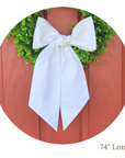 Green wreath with a white linen wreath sash tied in a bow on a wooden background, 74 inches long.