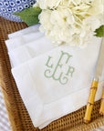 set of white linen dinner napkins with embroidered monogram in celadon green displayed on a woven tray with hydrangeas and chinoiserie jar