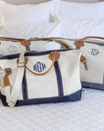 Custom, Embroidered Monogram Canvas Weekender Duffle Bag with navy trim and gray trim, sitting on a bed
