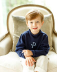 Child wearing navy cotton rollneck sweater with embroidered name detail