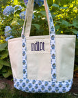 Canvas tote bag with block print accents and 'ndipt' monogram against a green leafy background