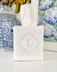 White tissue box cover with blue monogram 'L' on a surface with decorative items in the background.