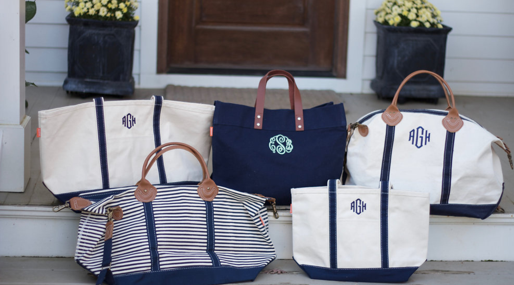 Assortment of personalized canvas travel bags and totes with navy trim and embroidered monograms styled on front porch steps.
