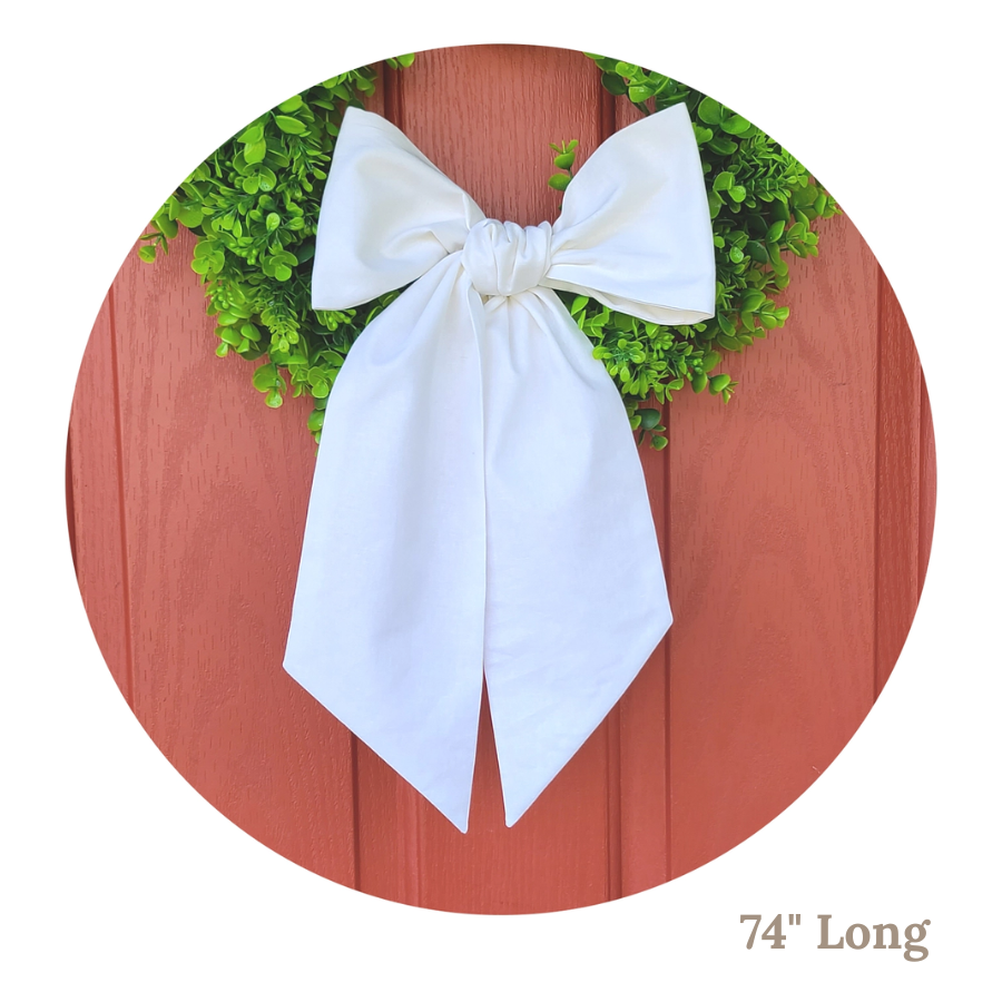 Green wreath with a white linen wreath sash tied in a bow on a wooden background, 74 inches long.