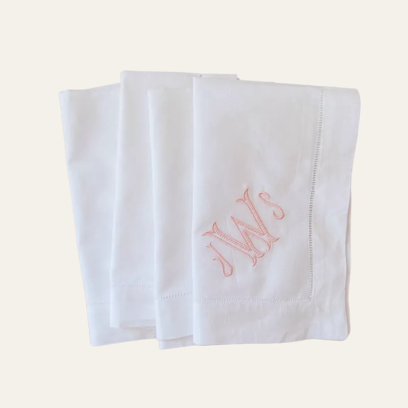 set of 4 white linen dinner napkins with embroidered monogram initials in heirloom blush thread on beige background