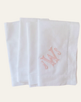 set of 4 white linen dinner napkins with embroidered monogram initials in heirloom blush thread on beige background