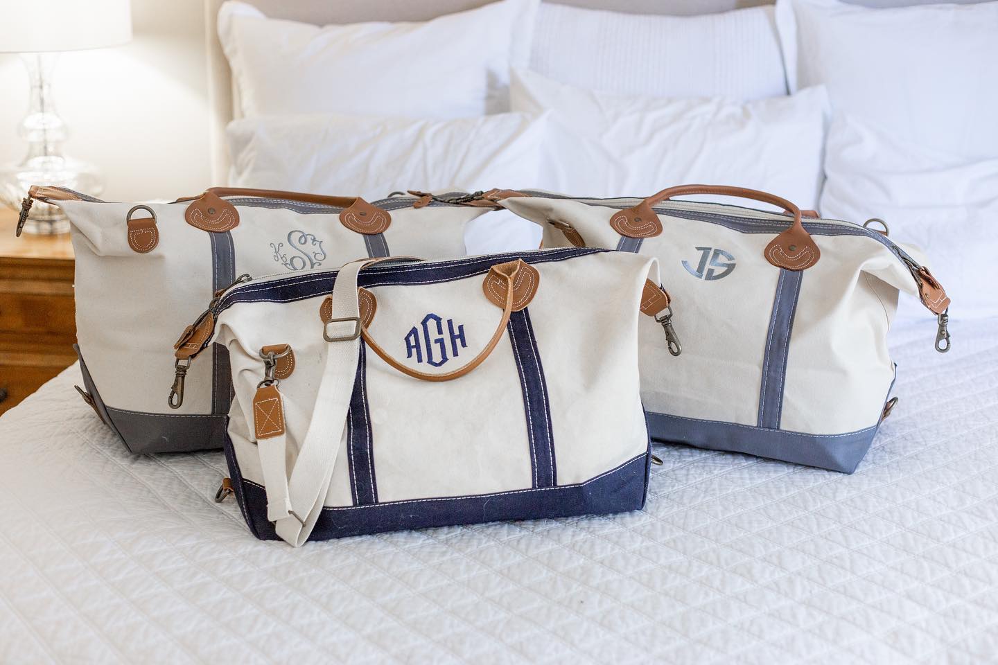 Custom, Embroidered Monogram Canvas Weekender Duffle Bag with navy trim and gray trim, sitting on a bed