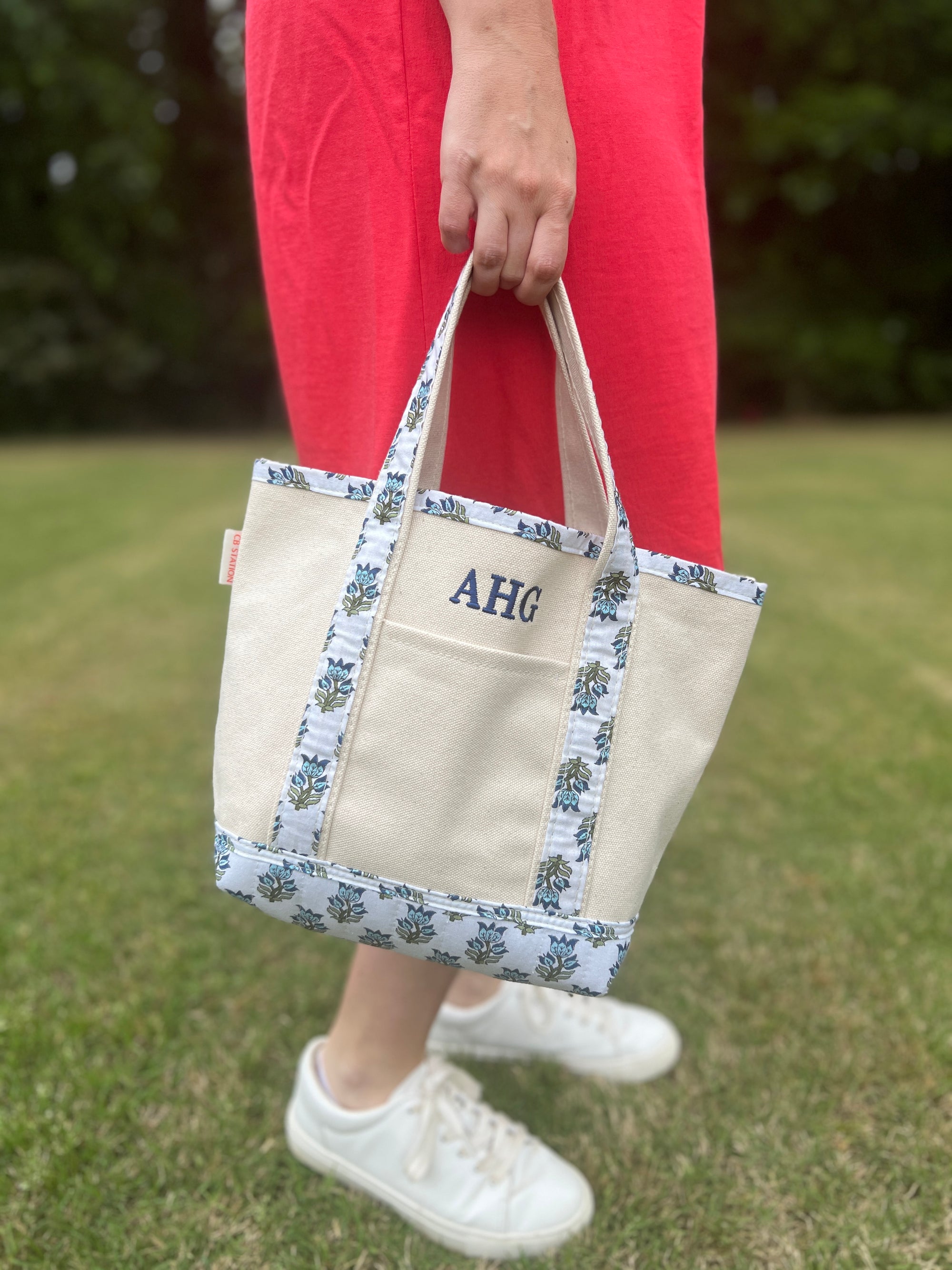 person carrying canvas tote bag with monogrammed initials featuring block print trim