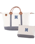 White and gray weekender travel bag with brown handles and blue monogram on a white background