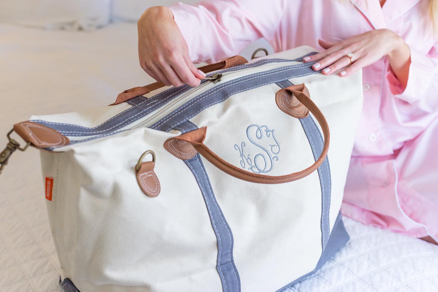 Canvas weekender travel bag with newlywed unzipping it featuring a personalized monogram