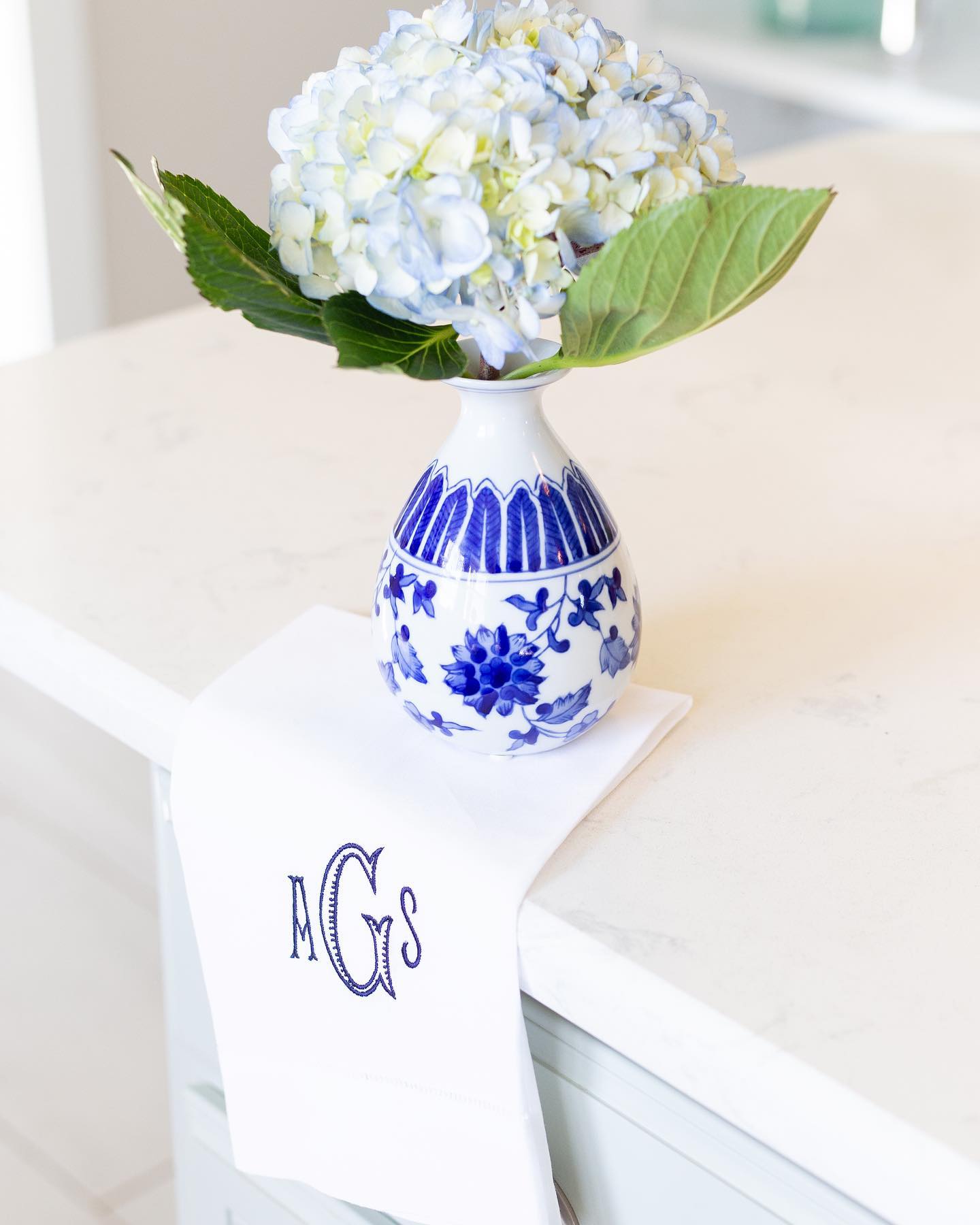 Blue and white ceramic vase with hydrangeas on a surface with a monogram linen guest towel