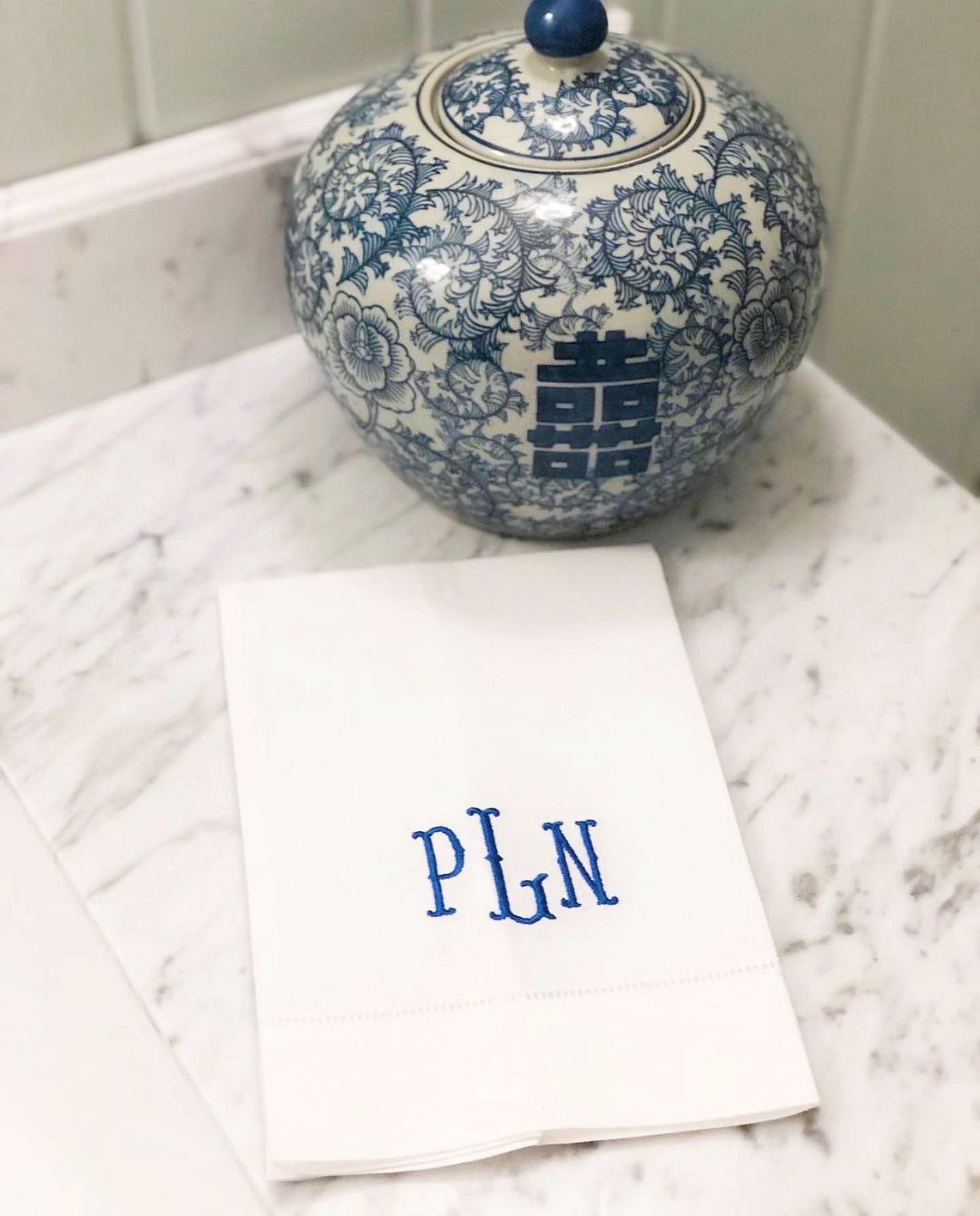 Blue and white decorative jar with floral patterns on a marble surface with a white linen guest towel with an embroidered monogram.
