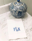 Blue and white decorative jar with floral patterns on a marble surface with a white linen guest towel with an embroidered monogram.