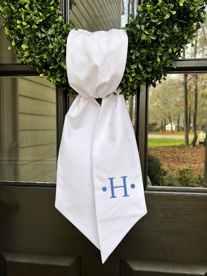 white linen wreath sash on boxwood wreath hanging on a front door with embroidered personalized initials