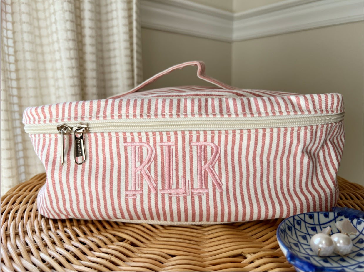 Personalized pink striped canvas cosmetic case with embroidered monogram styled on table.